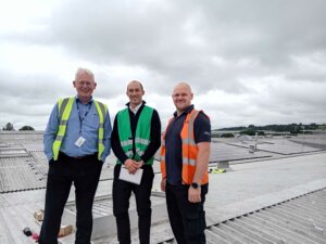 Picture showing three people standing on roof with solar panels in the background.