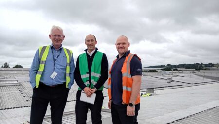 Picture showing three people standing on roof with solar panels in the background.