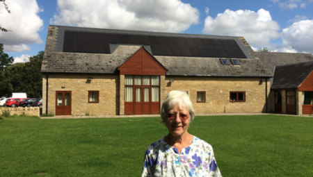 Celia Hawkesworth of Sustainable Kirtlington, standing outside Kirtlington Village Hall with its solar panels installed