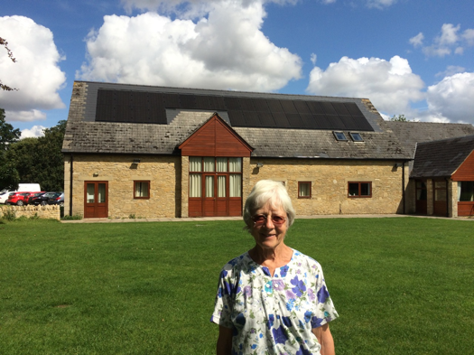 Celia Hawkesworth of Sustainable Kirtlington, standing outside Kirtlington Village Hall with its solar panels installed