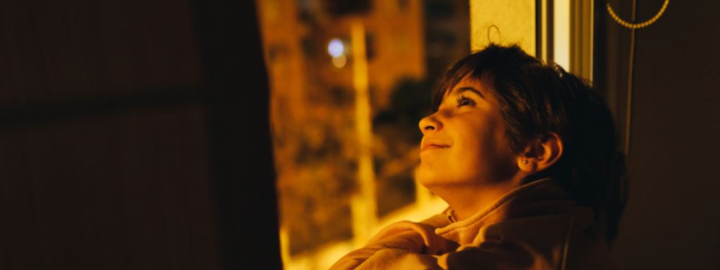 A young boy looks up at the stars through an open window.