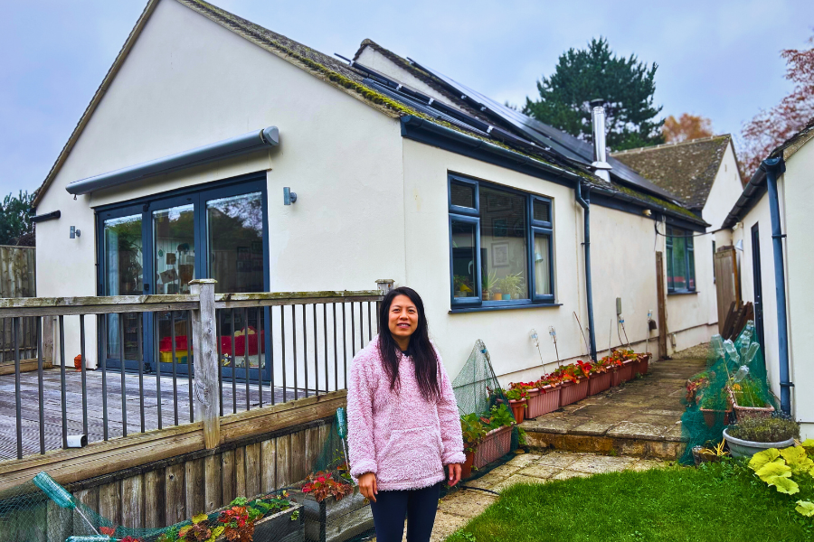 A sustainable homeowner poses under solar panels outside a bungalow building.
