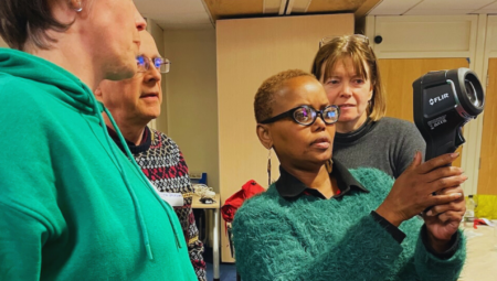 A lady holds a thermal imaging camera and receives guidance from other members of a thermal imaging event.