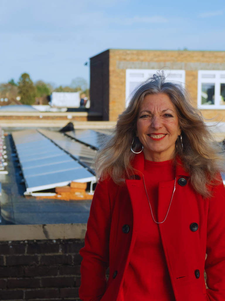 A happy teacher posing in front of a rootfop solar panel installation on a school rooftop.